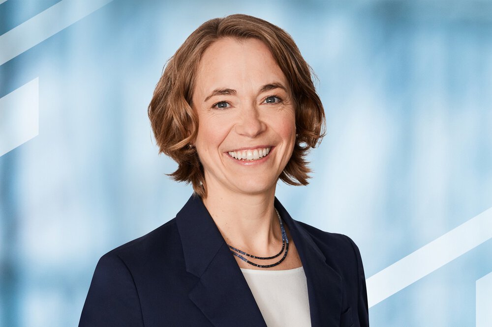 Brightly smiling woman with short, wavy hair in a dark blue suit over a white top.